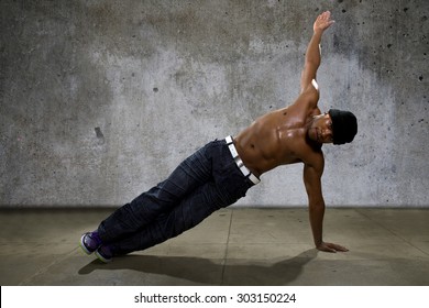 Man Demonstrating Core Balance Exercises Or Yoga On Urban Background. He Is Dressed In Hip Hop Style Clothing But Shirtless To Show Off Muscles.