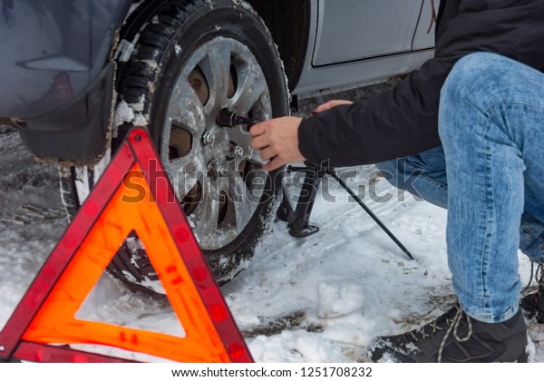 Man demontaging a car wheel on a snow road.\
Еmergency sign