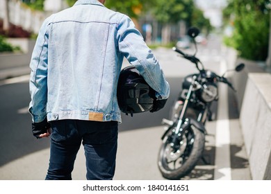 Man In Denim Jacket Standing With Motorcycle Helmet, View From The Back