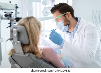 Man dentist in face mask and glasses doing treatment for patient blonde lady, holding dental tools, wearing rubber gloves. Stomatology, dentistry, modern dental clinic concept - Shutterstock ID 1999329833