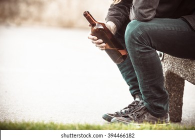 Man depressed with wine bottle sitting on bench outdoor. People abuse and alcoholism problems. - Shutterstock ID 394466182