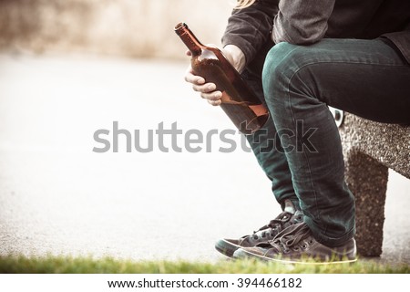 Man depressed with wine bottle sitting on bench outdoor. People abuse and alcoholism problems.