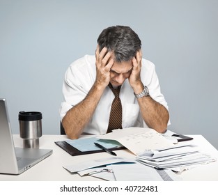 Man at desk in shirt and tie holding his head and worrying about money. - Powered by Shutterstock