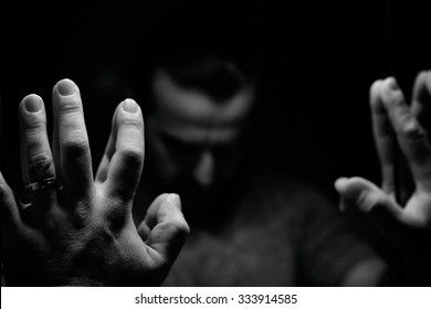 Man in despair with raised hands and bowed hand, monochromatic image in a low light room looking in front of mirror