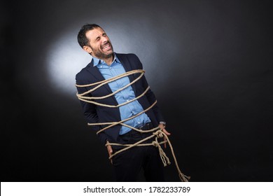 Man in desperate suit screams tied with a rope over a chair isolated on a black background