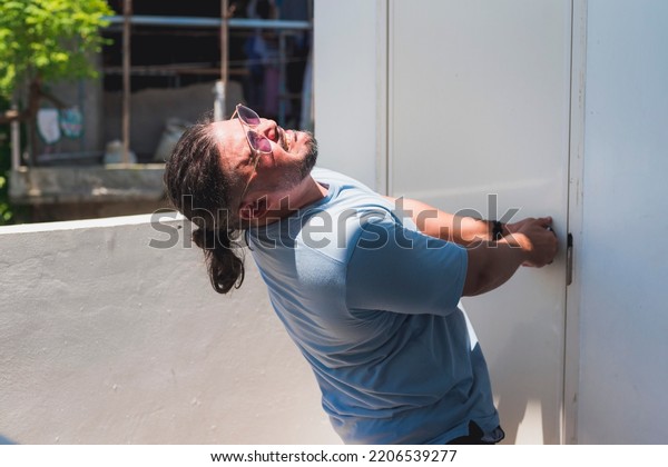 A man desperately pulls on a locked door in a\
futile attempt to get inside the public restroom. Pulling with all\
his might and bodyweight.