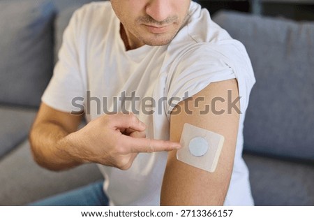 Man with diabetes patch sensor on arm. He points to a wearable glucose monitor, highlighting modern health tracking and convenient management at home. Healthcare monitoring and diabetic control.