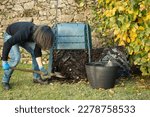 A man is digging and loading ready compost from a outdoor compost bin to use in the garden. The compost bin is placed in a home garden to recycle organic waste produced in home and garden. 