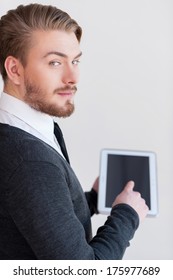 Man With Digital Tablet. Rear View Of Handsome Young Man Holding A Digital Tablet And Looking Over Shoulder While Standing Against Grey Background