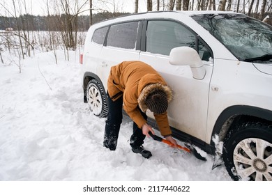 A man digs out a stalled car in the snow with a car shovel. Transport in winter got stuck in a snowdrift after a snowfall, sat on the bottom. First aid, tow truck, winter tires spikes and all-season - Powered by Shutterstock