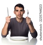 Man at dinner table with fork and knife raised. Hunger strike isolated over white background