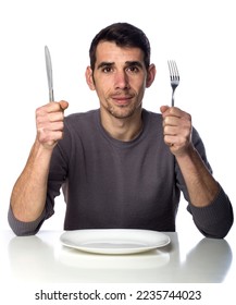 Man at dinner table with fork and knife raised. Hunger strike isolated over white background