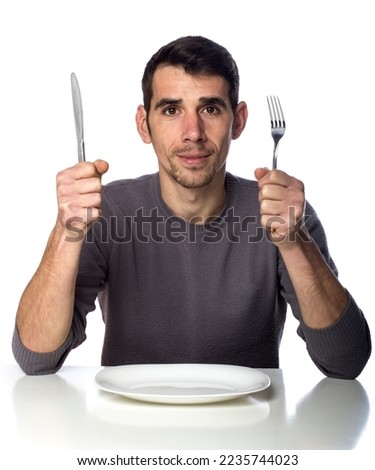 Man at dinner table with fork and knife raised. Hunger strike isolated over white background