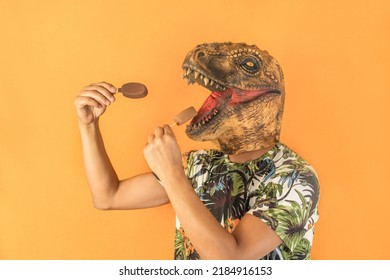 Man In Dinosaur Animal Head Mask Eating Two Chocolate Ice Creams Isolated On Yellow Background With Copy Space