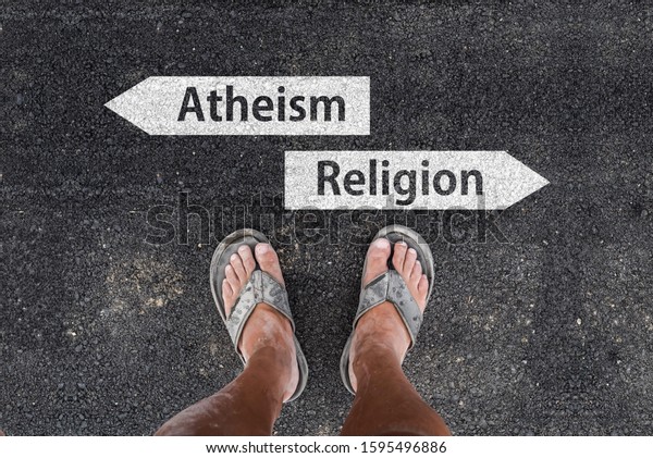 man with dirty feet\
in slippers is standing on asphalt next to arrow signs of words\
atheism and religion