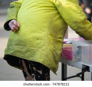 Man In Dirty Yellow High Vis Coat And Camouflage Pants Selects Items From Market Stall