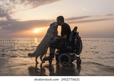 Man with disability, electric wheelchair user petting his dog and enjoying a sunset on the beach. People and animal friendship concept. - Powered by Shutterstock