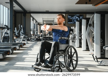 Man with disability stretching arms while sitting in wheelchair at gym, exercising for rehabilitation and wellbeing