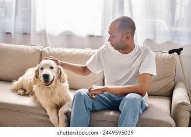 A man, disabled with myasthenia gravis, sits on a sofa petting a Labrador dog, showcasing diversity and inclusion. - Powered by Shutterstock