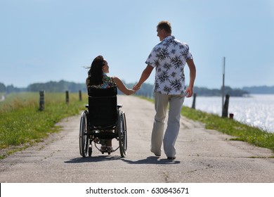 Man and disabled woman walking outdoor hand in hand looking at each other - day light - wheelchair user and her loving husband, view from behind - Powered by Shutterstock