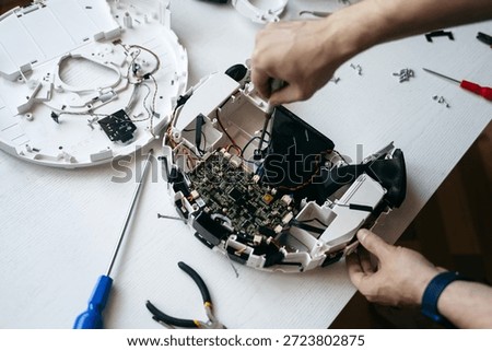 A man disassembles a vacuum cleaner and takes out the microcircuits. Disassembled robot vacuum cleaner. Replacement of spare parts. Damaged vacuum cleaner for repair. Burnt chip, board. Device diagnostics. Close macro photo.