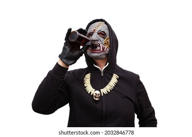 A man disguised in a zombie mask wearing a black hooded sweatshirt with a hood is drinking a beer from a glass bottle.