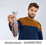 Man, disgust and fish with bad smell, odor or stink of animal or sea creature on a white studio background. Male person with gross facial expression of disgusted scent or smelly odd stench on mockup