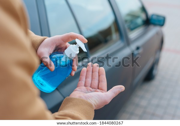 A man disinfects his hands in a parking lot\
with a car in the background