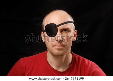 A man displays a serious expression while wearing an eye patch in front of a dark backdrop.