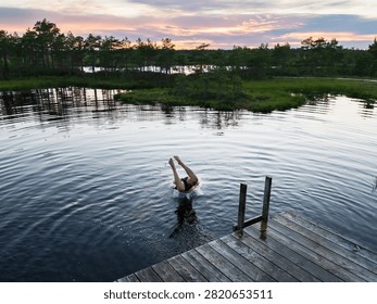 Man diving headfirst into bog lake from wooden pier during sunset in Estonian nature reserve outdoor summer swimming active lifestyle travel background.