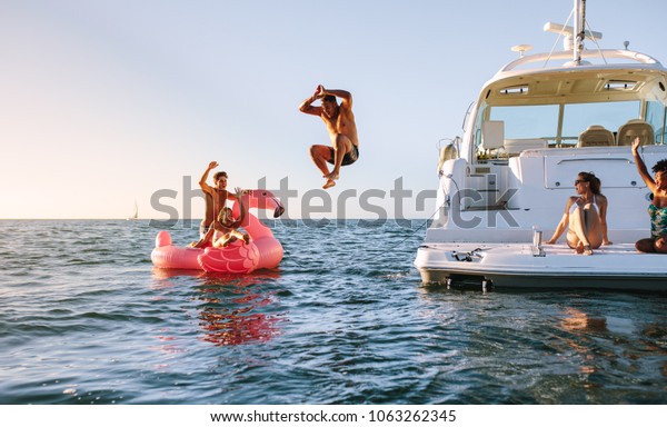 Man diving in the sea with friends sitting on\
yacht and inflatable toy. Group of friends enjoying a summer day on\
a inflatable toy and yacht.