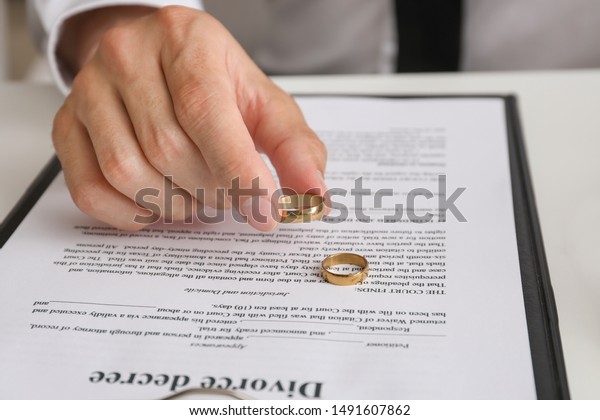 Man with divorce decree and rings sitting at\
table in lawyer\'s office,\
closeup