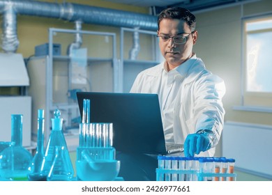 Man doctor in laboratory. Researcher with laptop and flasks. Table with test tubes near laboratory assistant. Scientist in industrial laboratory. Man corrects scientific experiment.
