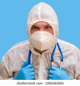 Man Doctor Medic In A Protective Suit Uniform With Goggles And Face Mask On A Studio Blue Background. Paramedic In White Antiviral Protective Clothing Wearing An N95 Respirator And Safety Glasses