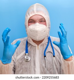 Man Doctor Medic In A Protective Suit Uniform With Goggles And Face Mask On A Studio Blue Background. Paramedic In White Antiviral Protective Clothing Wearing An N95 Respirator And Safety Glasses