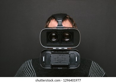 Man does not correctly use virtual reality glasses, gray background.