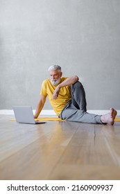 A Man Does Yoga And Fitness In The Gym With A Trainer Online From A Laptop. Senior Male Sports Coach On The Internet. Senior Yoga At Home Or In The Gym For Training. A Fifty-year-old Man With Gray