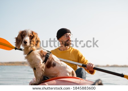 Man with a dog in a canoe on the lake. Young male person with spaniel in a kayak row boat, active free time with pets, companionship, adventure dogs