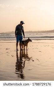 Man And Dog German Shepherd Playing On Remote Empty Beach Avoiding People To Keep Social Distancing. Owner With Pet Off Leash Running Free At Dog Friendly Beach. Outdoors, Pets And New Normal.