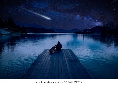 Man with dog looking at Perseid Meteor Shower at lake Bled