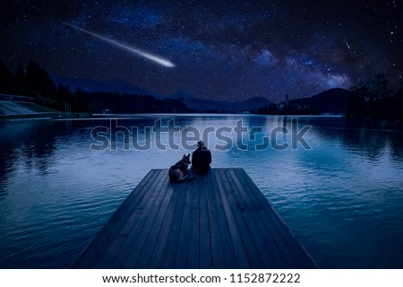 Man with dog looking at Perseid Meteor Shower at lake Bled