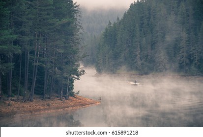 Man And Dog On A Boat In A Mystic Foggy Lake Near The Forest. Fisherman And Dog In Big Lake. A Misty Morning By The Lake. Small Fishing Boat At The Lake. Space For Text