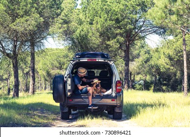 Man With Dog Sitting In Off Road Car Boot In Forest. Freedom And Traveling Couple.