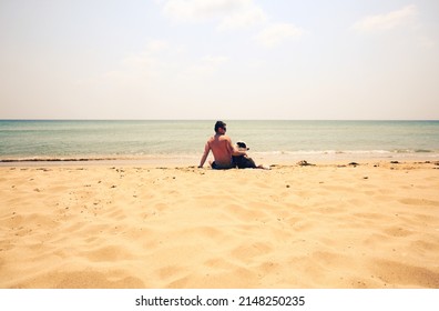 Man And Dog Sitting On Beach Near Sea. Vintage Retro Photo Effect.