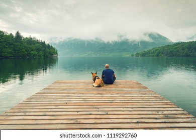 Man with dog sitting at wooden pier at Bohinj Lake, SLovenia. - Powered by Shutterstock