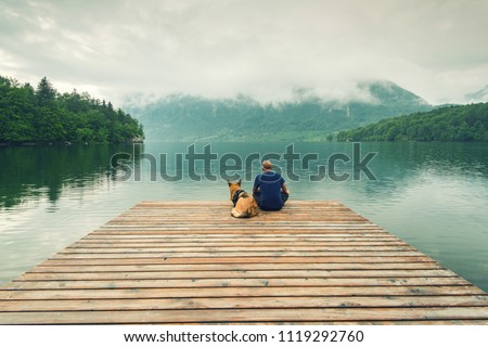 Man with dog sitting at wooden pier at Bohinj Lake, SLovenia.