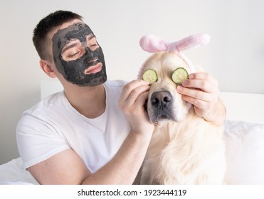 A man with a dog takes care of facial skin at home. A guy and a golden retriever put on a clay face mask. The concept of male health and beauty, cosmetology, body and skin care.