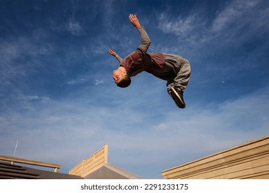 Man doing back somersault against blue sky. Parkour athlete training in city in sportive clothes. Free runner jumping have workout. Active lifestyle. Extreme sports, outdoor freerun