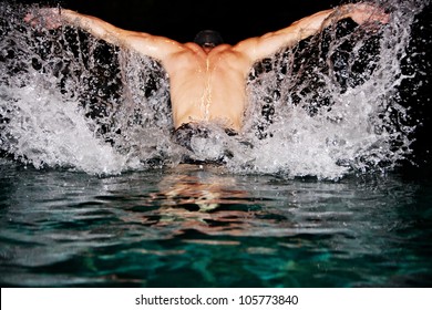 Man Doing Butterfly Strokes While Swimming In A Pool At Night. Dramatic Water Splashing.