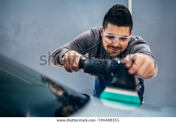 Man doing a car polish\
with a machine.